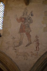 Wall painting of a shepherd dressed in red and blue tunic and hose surrounded by sheep, accompanied by a dog and small boy